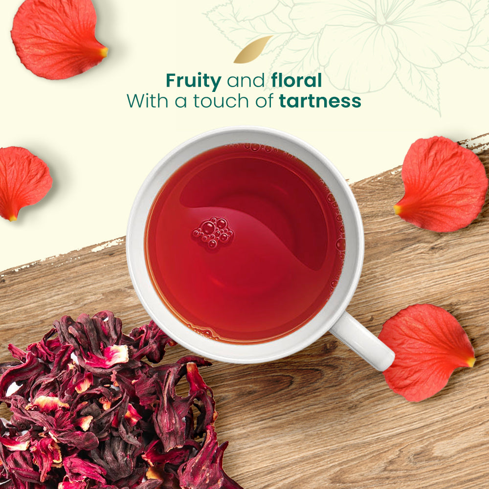 Cup of red hibiscus tea with dried hibiscus flowers and petals on a wooden surface.