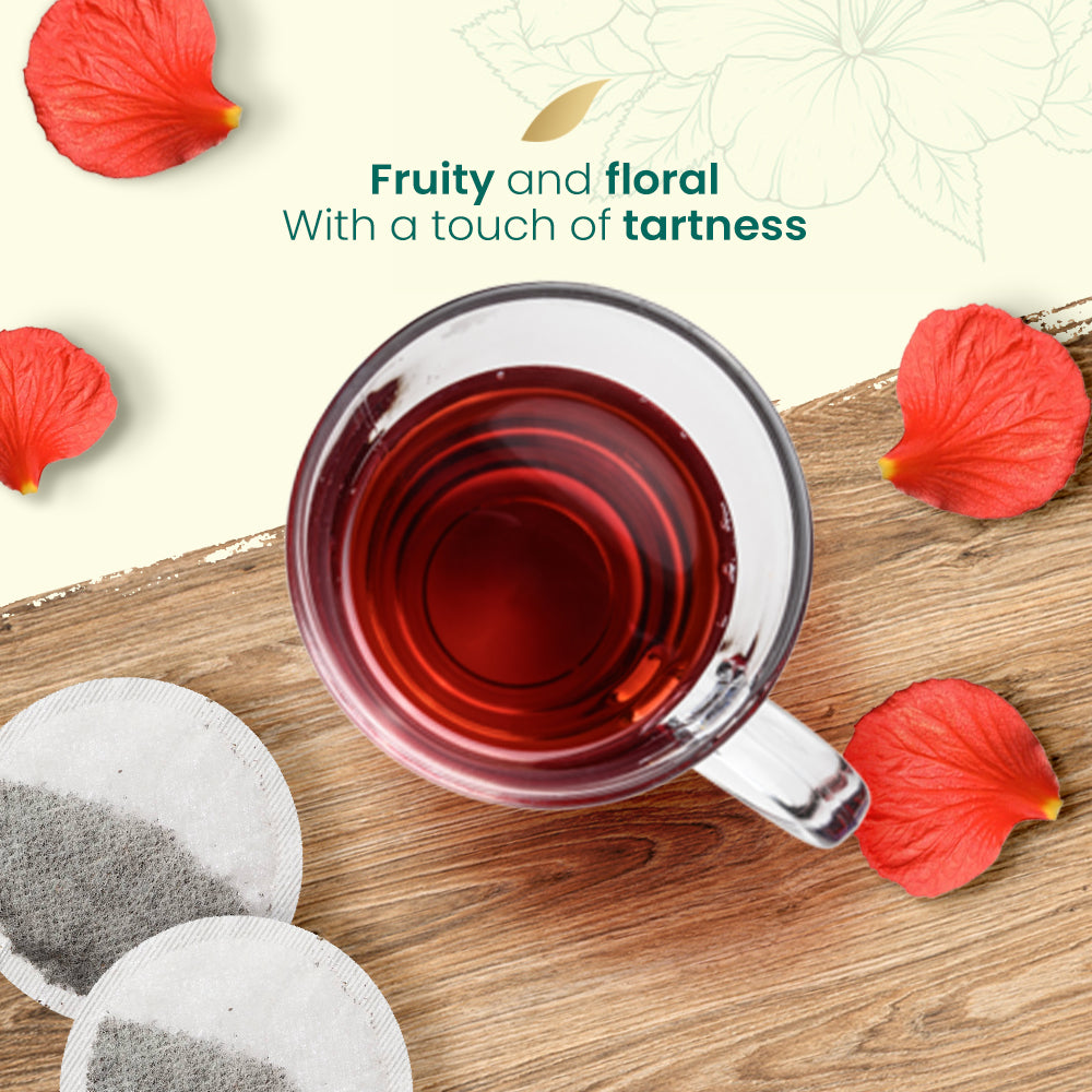 Cup of red hibiscus tea on a wooden surface with Natural Evity tea bags and hibiscus petals.