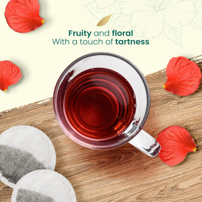 Cup of red hibiscus tea on a wooden surface with Natural Evity tea bags and hibiscus petals.